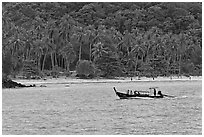 Longtail boat sailing in front of palm-fringed beach, Phi-Phi island. Krabi Province, Thailand (black and white)