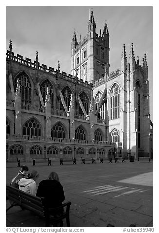 Young people sitting on a bench in a square below Bath Abbey. Bath, Somerset, England, United Kingdom