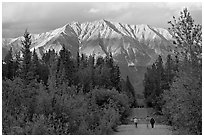 People walking on unpaved road, with last light on mountains. McCarthy, Alaska, USA (black and white)