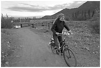 Woman on mountain bike with bridge behind. McCarthy, Alaska, USA (black and white)