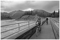 Mountain bikers crossing Kennicott River Footbridge at sunset. McCarthy, Alaska, USA (black and white)