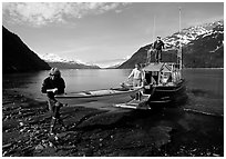 Man and woman carry kayak out of small boat at Black Sand Beach. Prince William Sound, Alaska, USA ( black and white)