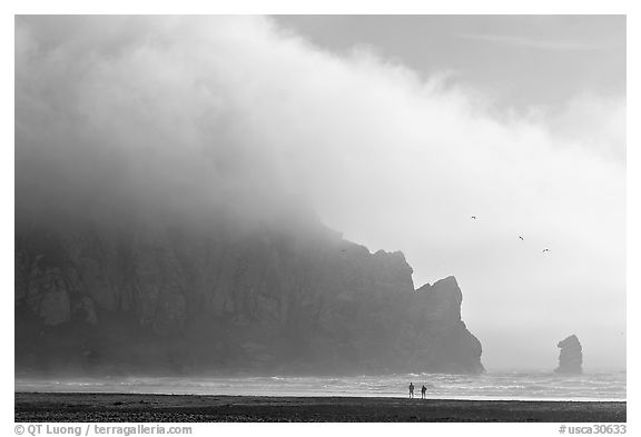 Two people strolling on the beach at the base of Morro Rock. Morro Bay, USA