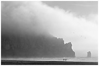 Two people strolling on the beach at the base of Morro Rock. Morro Bay, USA ( black and white)