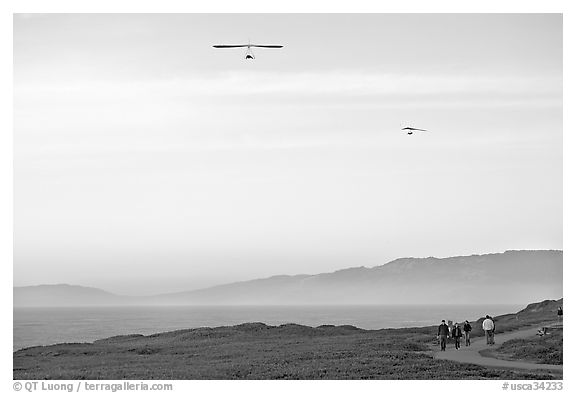 Hang gliders soaring above hikers, Fort Funston, late afternoon. San Francisco, California, USA