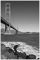 Surfer scrambling on rocks below the Golden Gate Bridge. San Francisco, California, USA (black and white)