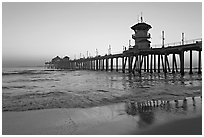 Huntington Pier reflected in wet sand at sunset. Huntington Beach, Orange County, California, USA ( black and white)