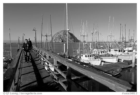 People walking on a deck in the harbor. Morro Bay, USA (black and white)