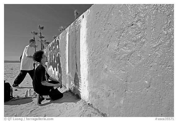 Young men creating graffiti art on a wall on the beach. Venice, Los Angeles, California, USA