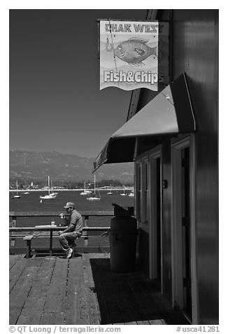 Man eating on wharf next to Fish and Chips restaurant. Santa Barbara, California, USA