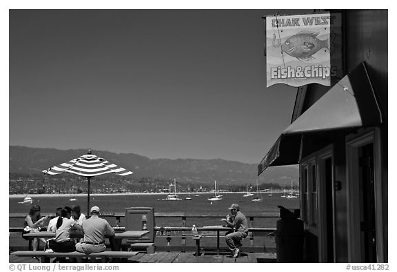 People eating with yachts and beach in background. Santa Barbara, California, USA (black and white)