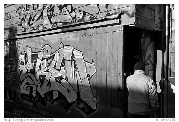 Man opening door of painted garage, Mission District. San Francisco, California, USA (black and white)