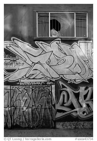 Mural paintings below broken window, Mission District. San Francisco, California, USA (black and white)