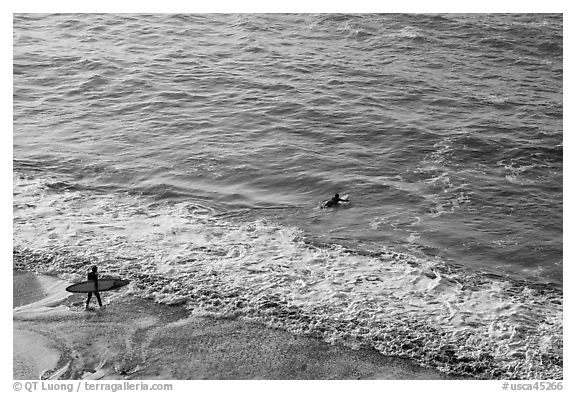 Surfers departing the beach towards the break. Half Moon Bay, California, USA (black and white)