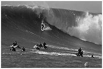 Surfer down huge wall of water observed from jet skis. Half Moon Bay, California, USA ( black and white)
