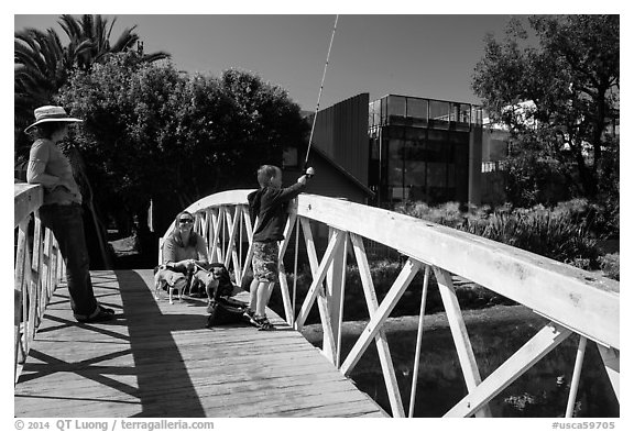 Boy fishing from arched bridge, Venice Canal Historic District. Venice, Los Angeles, California, USA (black and white)