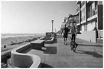 Couple walking dog on beachfront promenade, Manhattan Beach. Los Angeles, California, USA ( black and white)