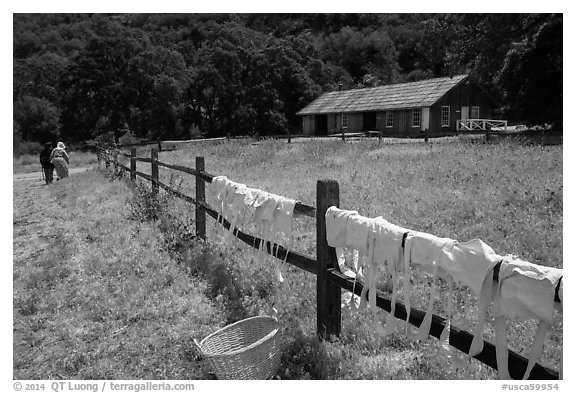 Laundry drying on fence, as elderly couple in period costume walks in distance, Fort Tejon. California, USA (black and white)