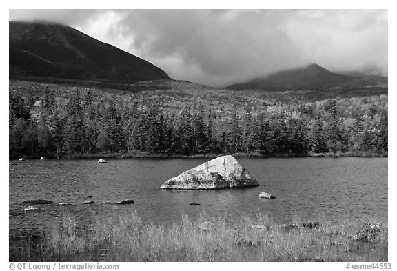 Boulder, pond, forest in autumn and mountains with clouds. Baxter State Park, Maine, USA (black and white)