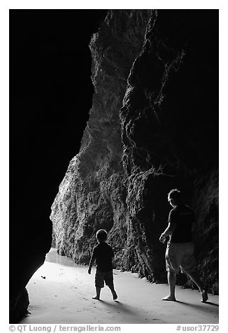 Father and son walking towards the light in sea cave. Bandon, Oregon, USA