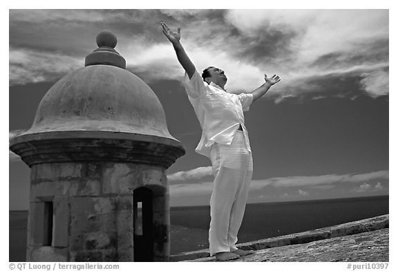 Man standing next to a lookout turret, with arms spread, El Morro Fortress. San Juan, Puerto Rico (black and white)