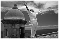 Man standing next to a lookout turret, with arms spread, El Morro Fortress. San Juan, Puerto Rico (black and white)