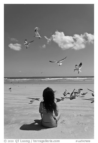 Girl sitting on beach with birds flying, Jetty Park. Cape Canaveral, Florida, USA (black and white)