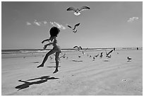 Girl jumping on beach with seagulls flying, Jetty Park. Cape Canaveral, Florida, USA (black and white)