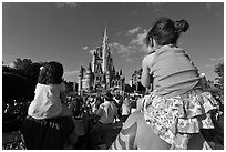 Toddlers sit on parent shoulders druing stage show. Orlando, Florida, USA (black and white)