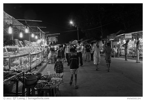 Shoppers walk past craft booth at night market. Phu Quoc Island, Vietnam (black and white)