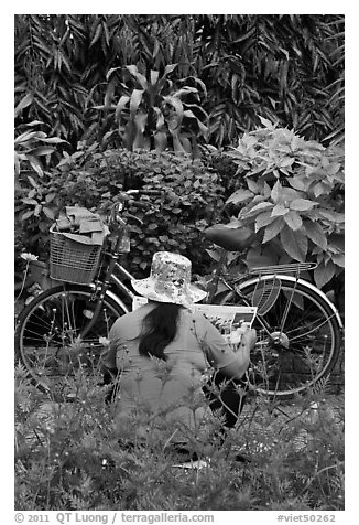 Woman reading newspaper next to bicycle in park. Ho Chi Minh City, Vietnam (black and white)