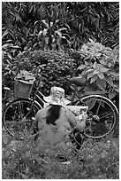 Woman reading newspaper next to bicycle in park. Ho Chi Minh City, Vietnam (black and white)