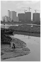 Man wading in mud, with background of towers in construction, Phu My Hung, district 7. Ho Chi Minh City, Vietnam (black and white)