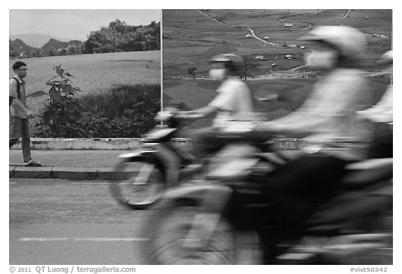 Man walking and motorbike riders blured in front of backdrops depicting traditional landscapes. Ho Chi Minh City, Vietnam