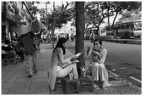 Women elegantly dressed in ao dai eating on the street. Ho Chi Minh City, Vietnam ( black and white)