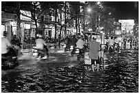Traffic passes man pushing food cart on flooded street at night. Ho Chi Minh City, Vietnam ( black and white)