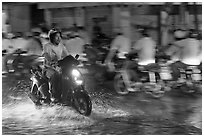 Man riding motorbike on flooded street seen against riders going in opposite direction. Ho Chi Minh City, Vietnam ( black and white)