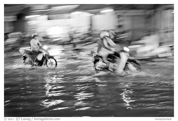 Motion-blured exposure of riders on flooded street at night. Ho Chi Minh City, Vietnam (black and white)