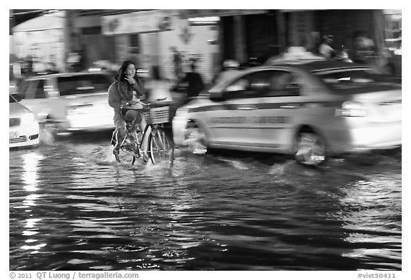 Women riding a bicycle on a flooded street at night. Ho Chi Minh City, Vietnam (black and white)
