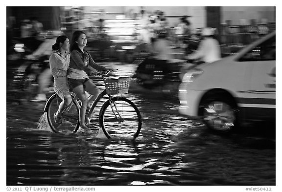 Women sharing a bicycle ride at night on a water-filled street. Ho Chi Minh City, Vietnam (black and white)