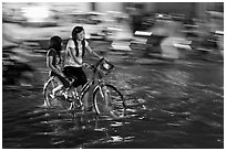 Girls sharing night bicycle ride through water of flooded street. Ho Chi Minh City, Vietnam ( black and white)