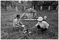Women burning notes as offering in cemetery. Ben Tre, Vietnam (black and white)
