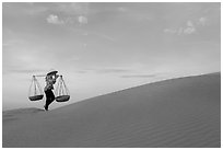 Woman with yoke baskets walks on sand dunes. Mui Ne, Vietnam ( black and white)