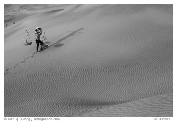 Woman walking with baskets on sands. Mui Ne, Vietnam (black and white)