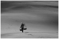 Woman walking on dune field with yoke baskets. Mui Ne, Vietnam ( black and white)