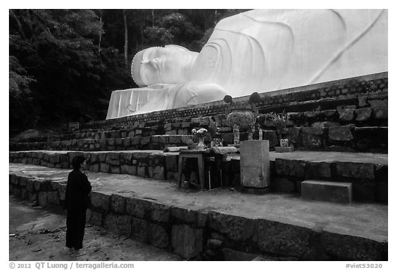 Woman prays below reclining Buddha statue. Ta Cu Mountain, Vietnam (black and white)