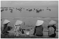 Four women in conical hats watch fishing activity from high above fishing village. Mui Ne, Vietnam ( black and white)