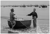 Man and woman gathering fishing net onto roundboat. Mui Ne, Vietnam ( black and white)