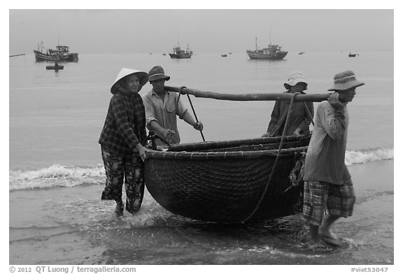 Fishermen carry round woven boat to shore. Mui Ne, Vietnam (black and white)