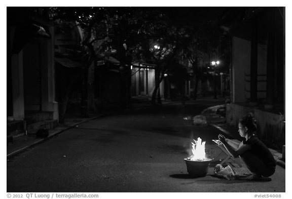 Woman burning paper on street at night. Hoi An, Vietnam (black and white)
